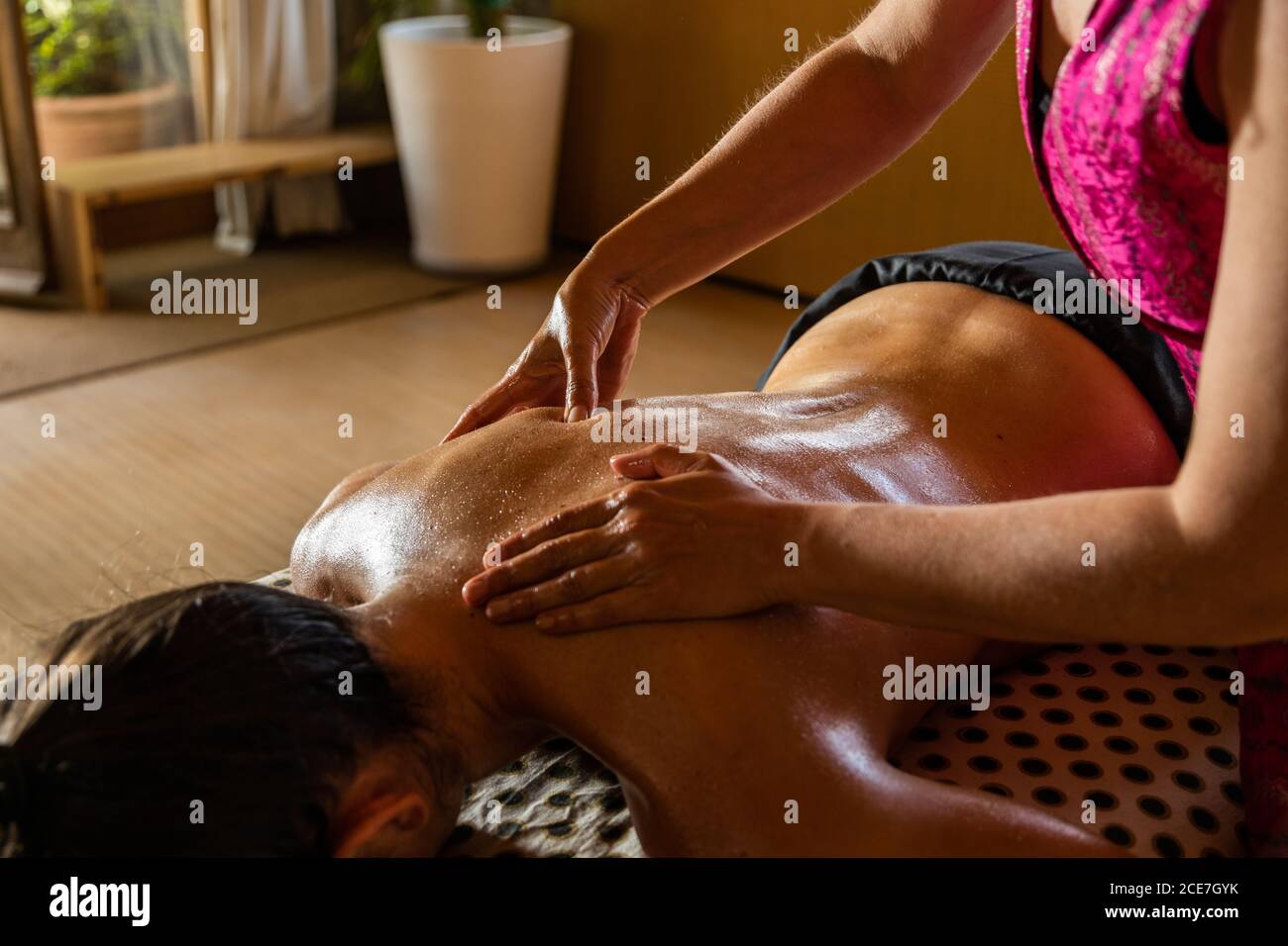 Crop anonimo master eseguire massaggio ayurvedico con olio aromatico ON retro di cliente rilassato in un salone moderno Foto Stock