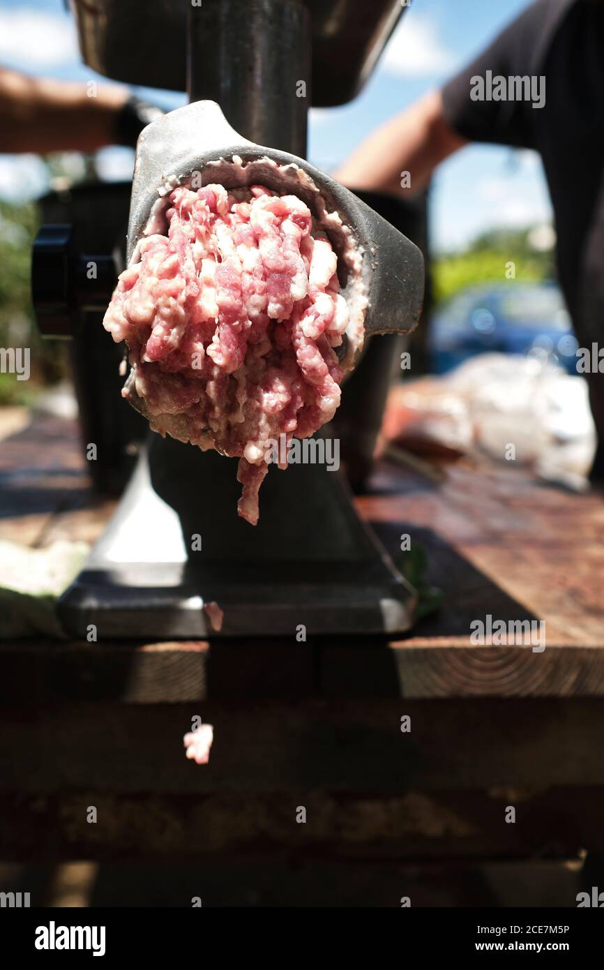 macellaio maschio non riconoscibile usando la macchina macinatrice mentre macina la carne a. fabbrica locale di macellazione Foto Stock