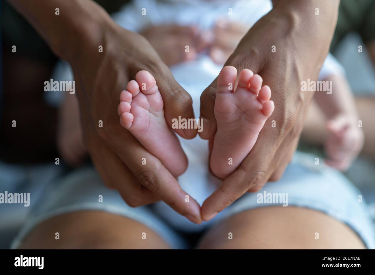 irriconoscibile pianta etnica madre che tiene i piedi minuscoli del bambino dentro forma del cuore mentre riposa a casa con il padre Foto Stock