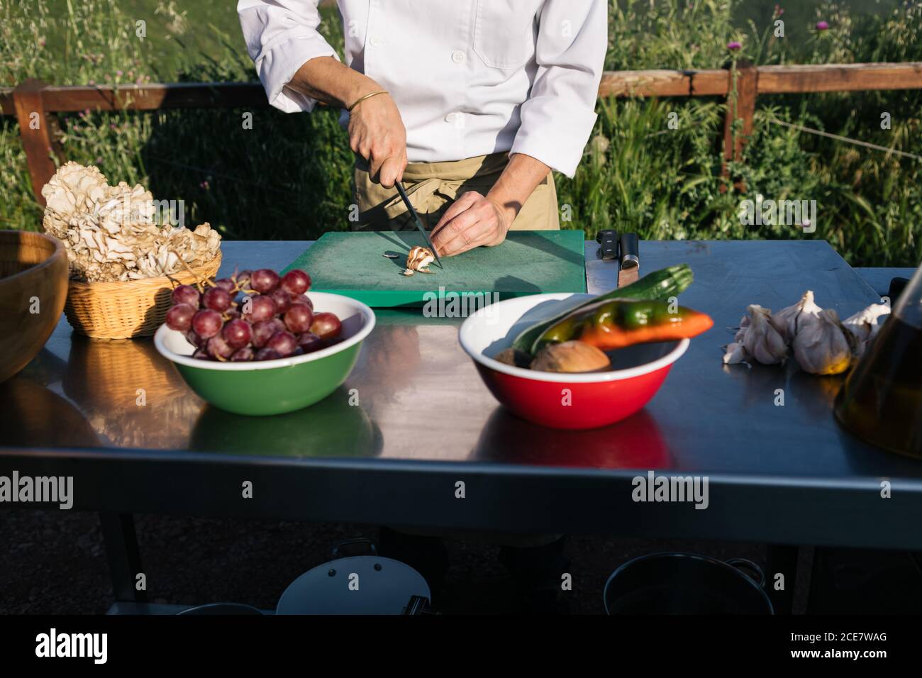 Dall'alto del raccolto inriconoscibile cuoco in tunica e grembiule tagliare le verdure durante la preparazione dell'insalata in un ristorante rustico all'aperto Foto Stock