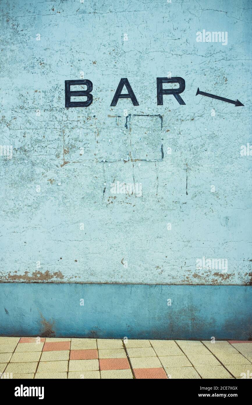 Vecchia parete blu in cemento con graffi sulla superficie e SULLA BARRA iscrizione con freccia dipinta vicino pavimento piastrellato nella luce del giorno Foto Stock