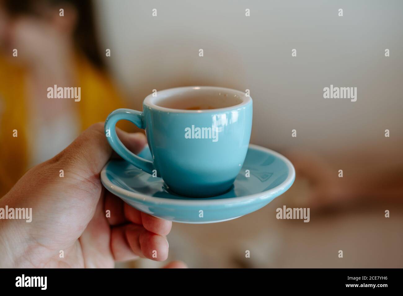 Crop persona irriconoscibile che tiene piatto di ceramica blu e tazza di tè aromatico caldo su sfondo sfocato nel caffè Foto Stock