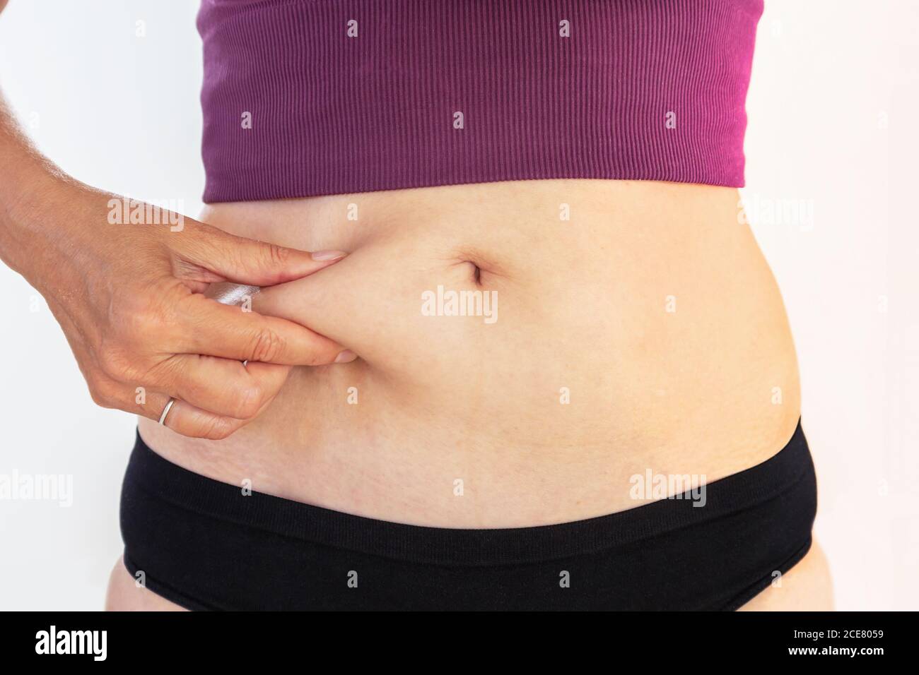 Donna matura pizzicando il suo grasso del ventre, cura del corpo e concetto di fitness Foto Stock