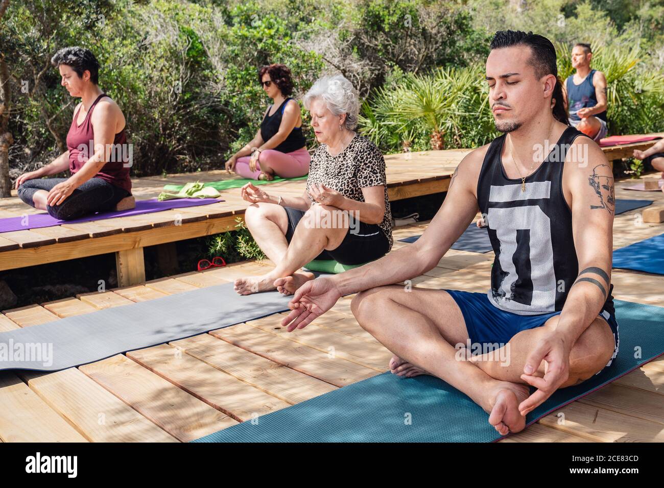 Giovane e anziano Donna in un gruppo di persone meditando in Lotus posa con gli occhi chiusi durante la pratica di yoga in località tropicale nelle giornate di sole Foto Stock