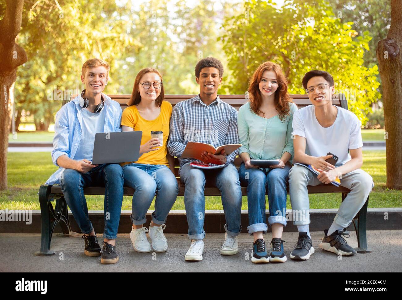 Gruppo di studenti multietnici che posano seduti sul banco di apprendimento all'esterno Foto Stock