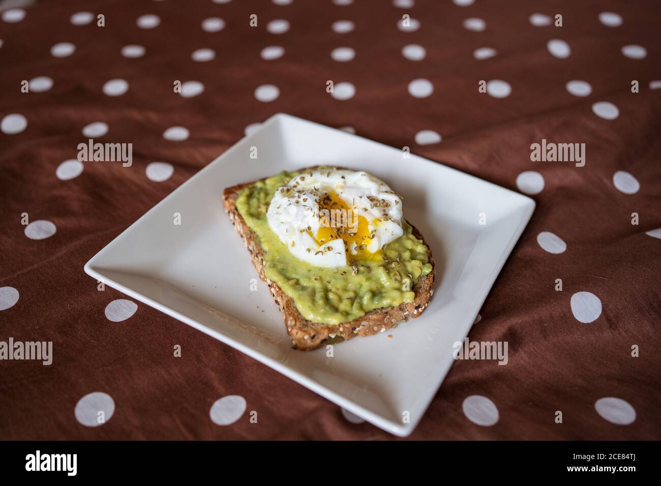 Appetitosa fetta di pane di grano con avocado e uovo in camicia sopra posizionato sulla piastra sul letto Foto Stock