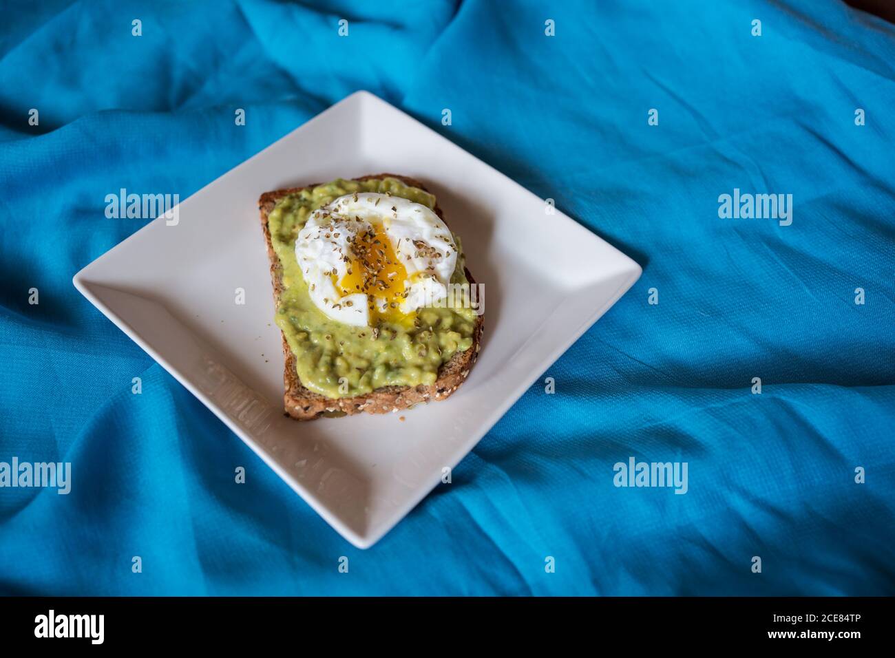 Appetitosa fetta di pane di grano con avocado e uovo in camicia sopra posizionato sulla piastra sul letto Foto Stock