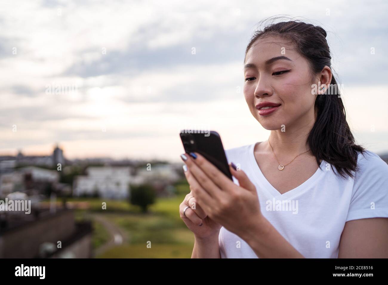 Donna che seleziona l'uomo mentre riposa sulla terrazza e sta navigando datando app sullo smartphone Foto Stock