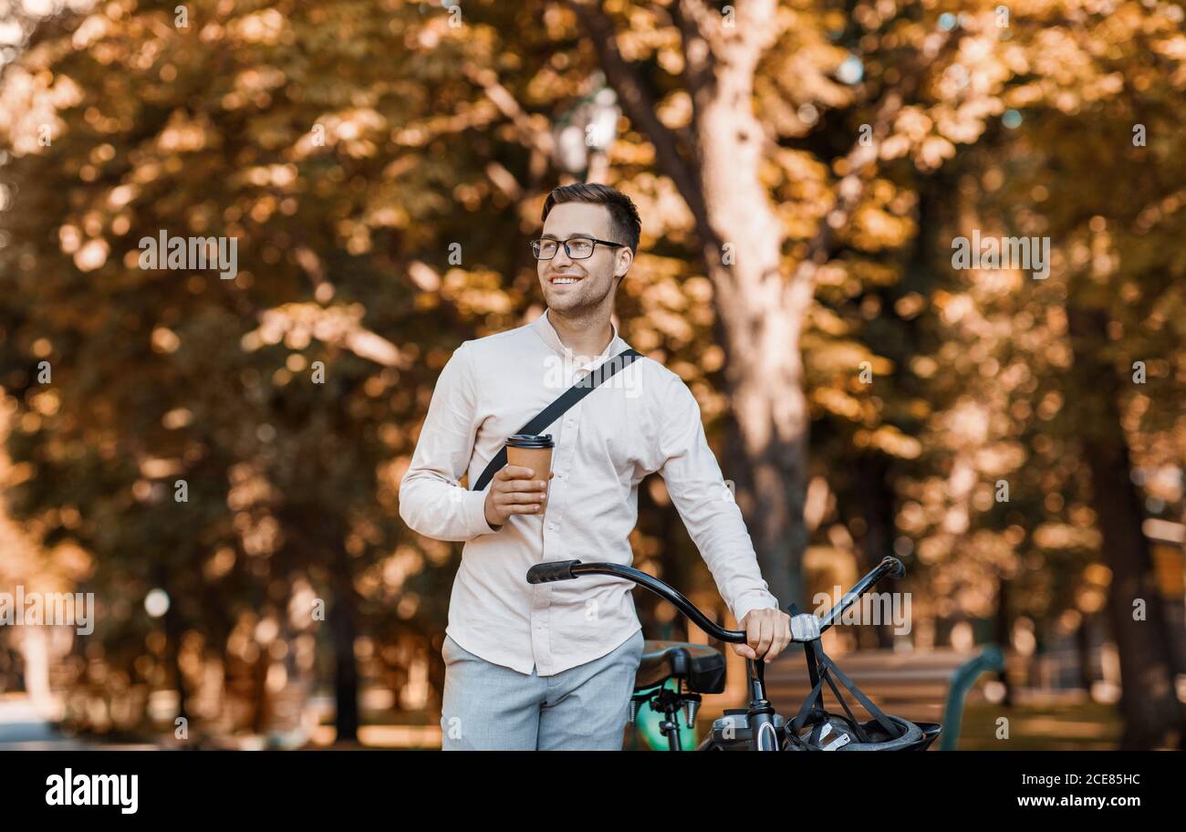 Stile di vita moderno e trasporto ecologico. Hipster felice che tiene il caffè e cammina con la bicicletta Foto Stock