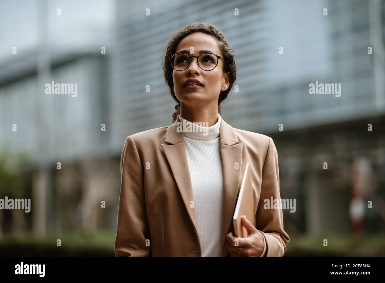 Donna d'affari che tiene un laptop che cammina all'aperto. Donna in formalwear e occhiali che camminano in città. Foto Stock