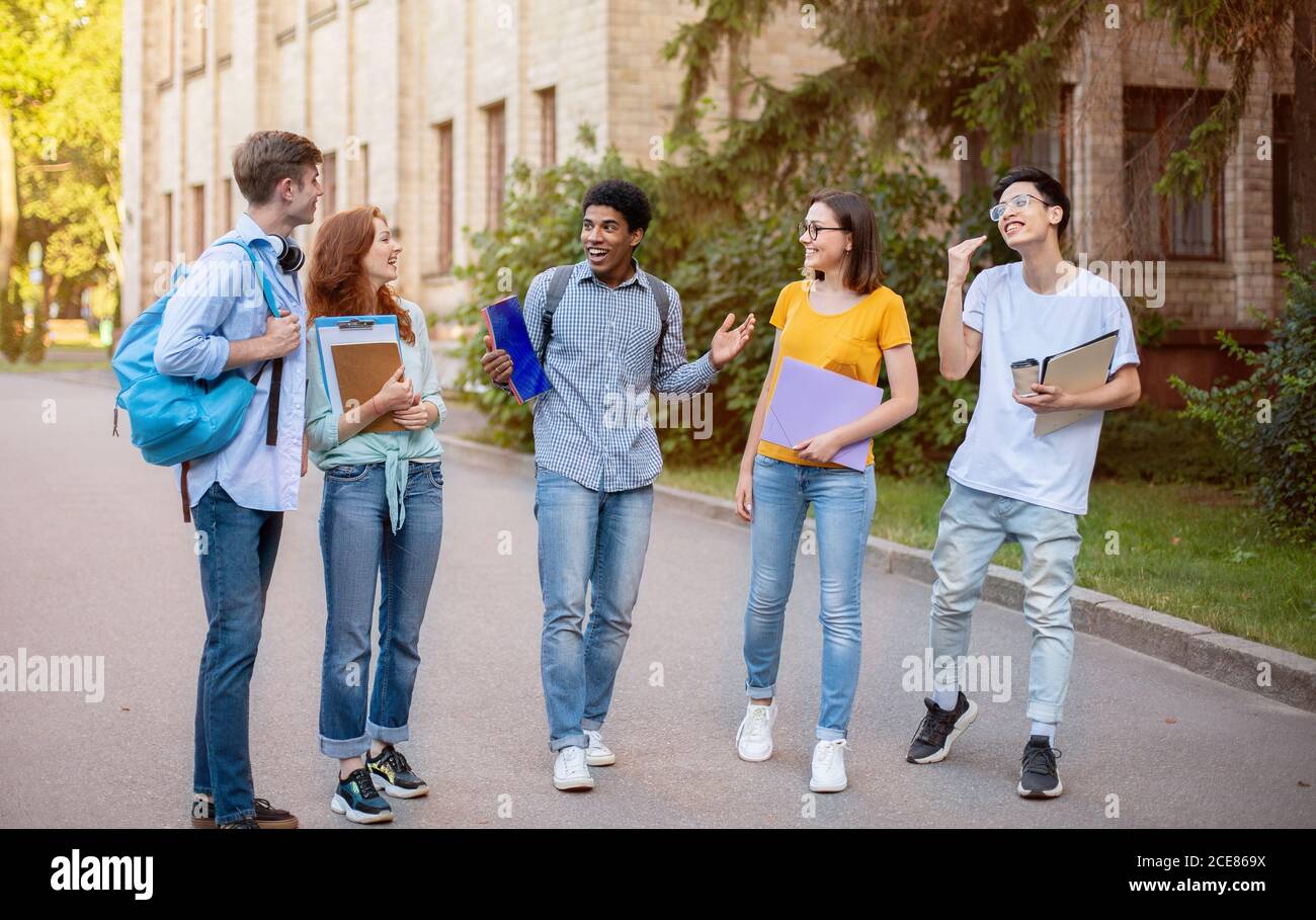 Studenti di Freshmen multietnici che parlano camminando all'esterno del campus universitario Foto Stock