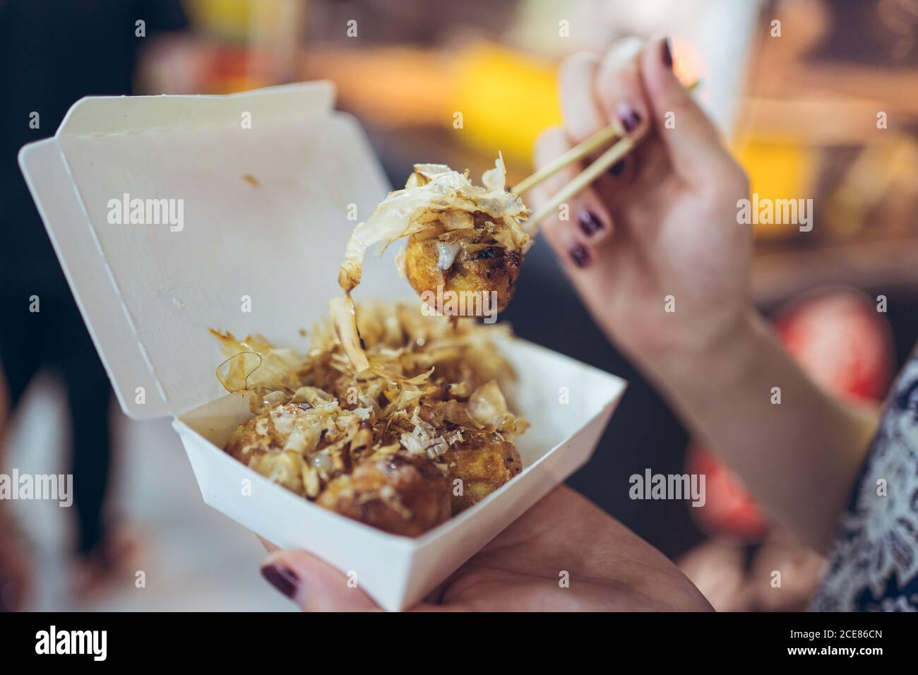 Crop femminile irriconoscibile in piedi nel mercato notturno di Zhubei e mangiare Deliziose palle di polpo Takoyaki Foto Stock