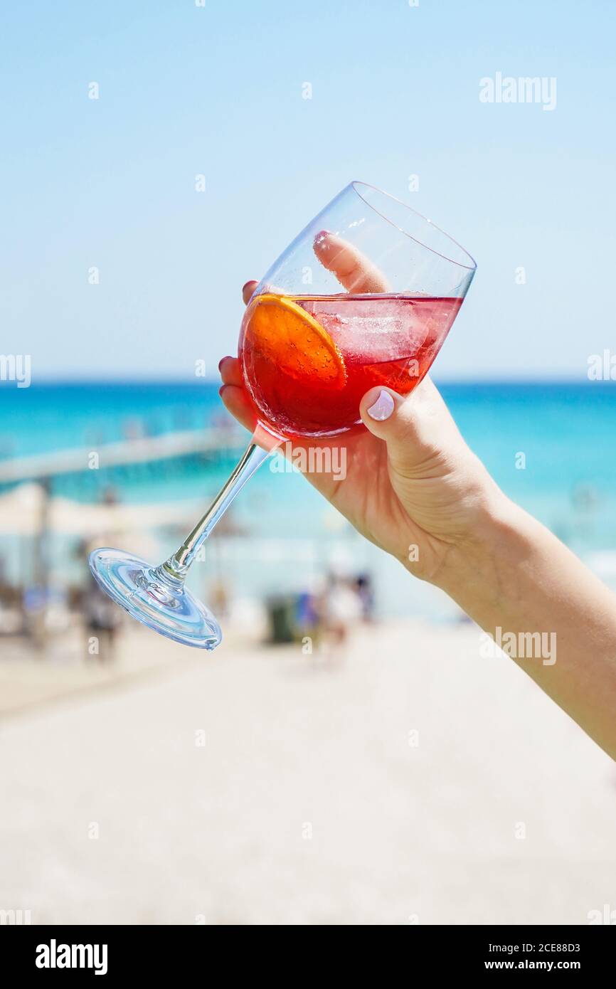 donna irriconoscibile che tiene il wineglass del cocktail alcolico rinfrescante degli agrumi mentre rilassarsi sulla spiaggia soleggiata in estate Foto Stock