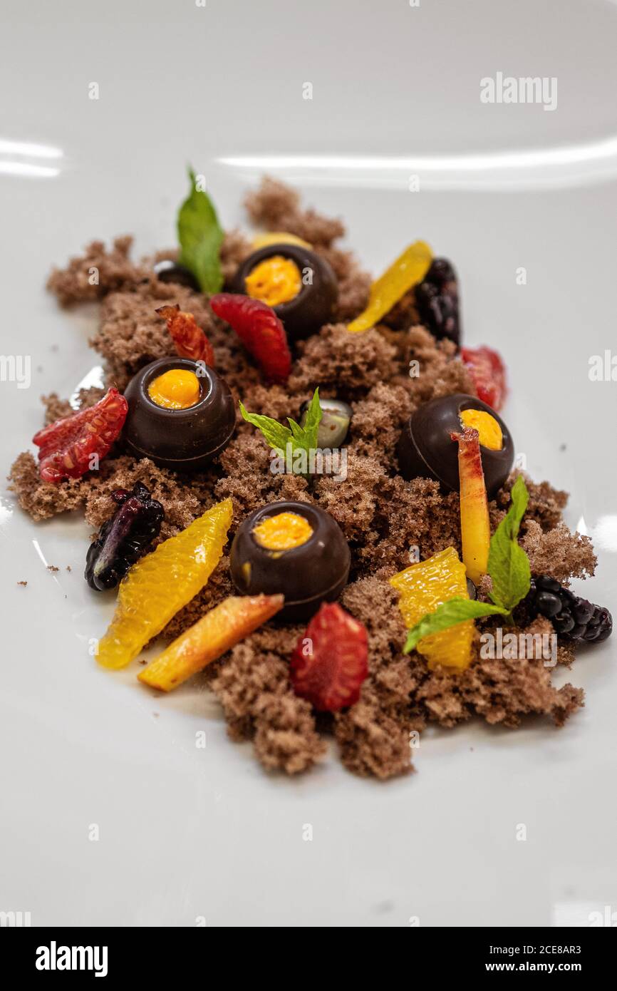 Da sopra delizioso dessert al cioccolato servito con pezzi di mango e foglie di fragola e menta sul piatto del ristorante Foto Stock