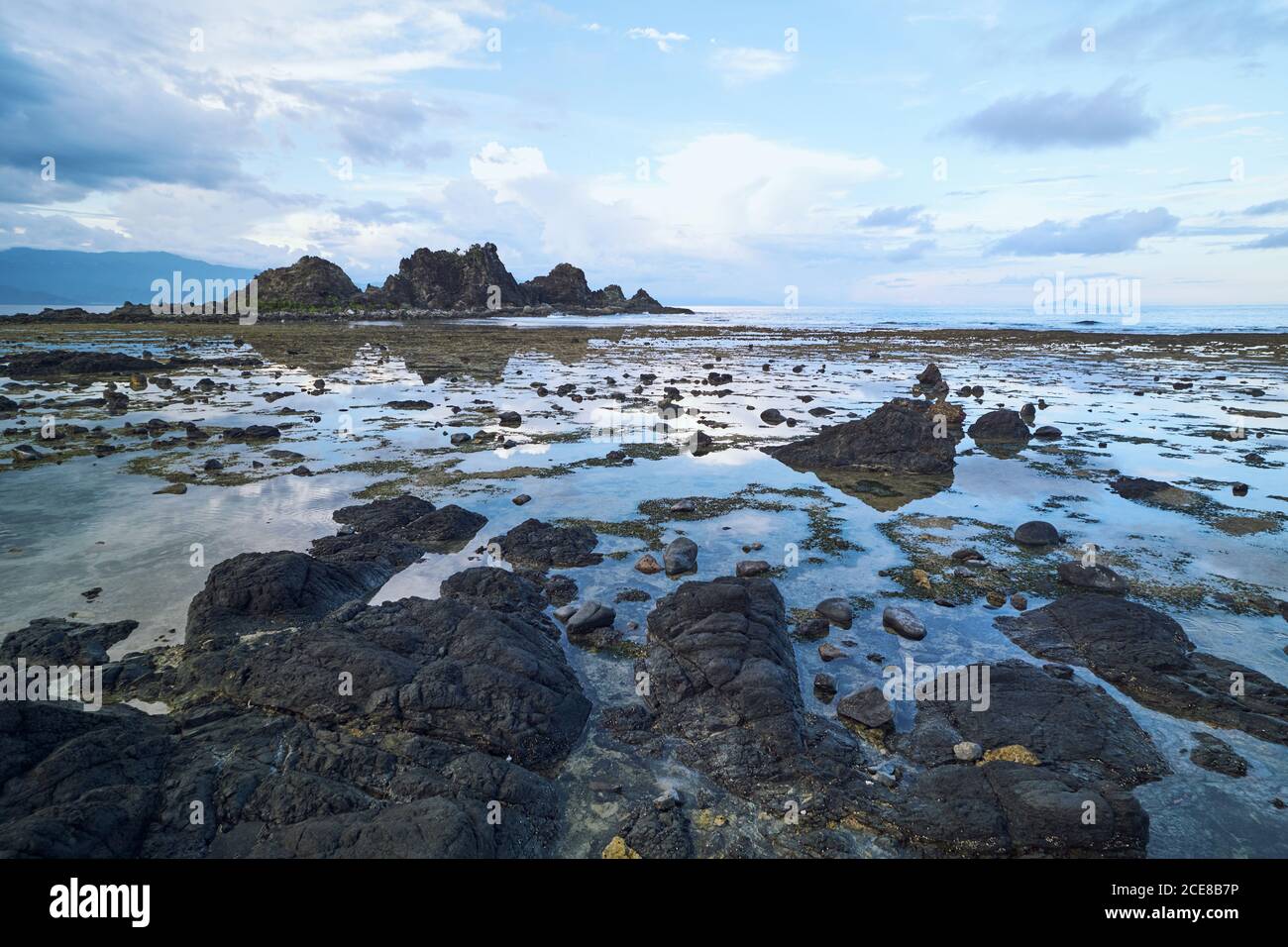 Scenario pittoresco di terreno sassoso con mare e alto rocce ripide sotto il cielo blu nuvoloso Foto Stock