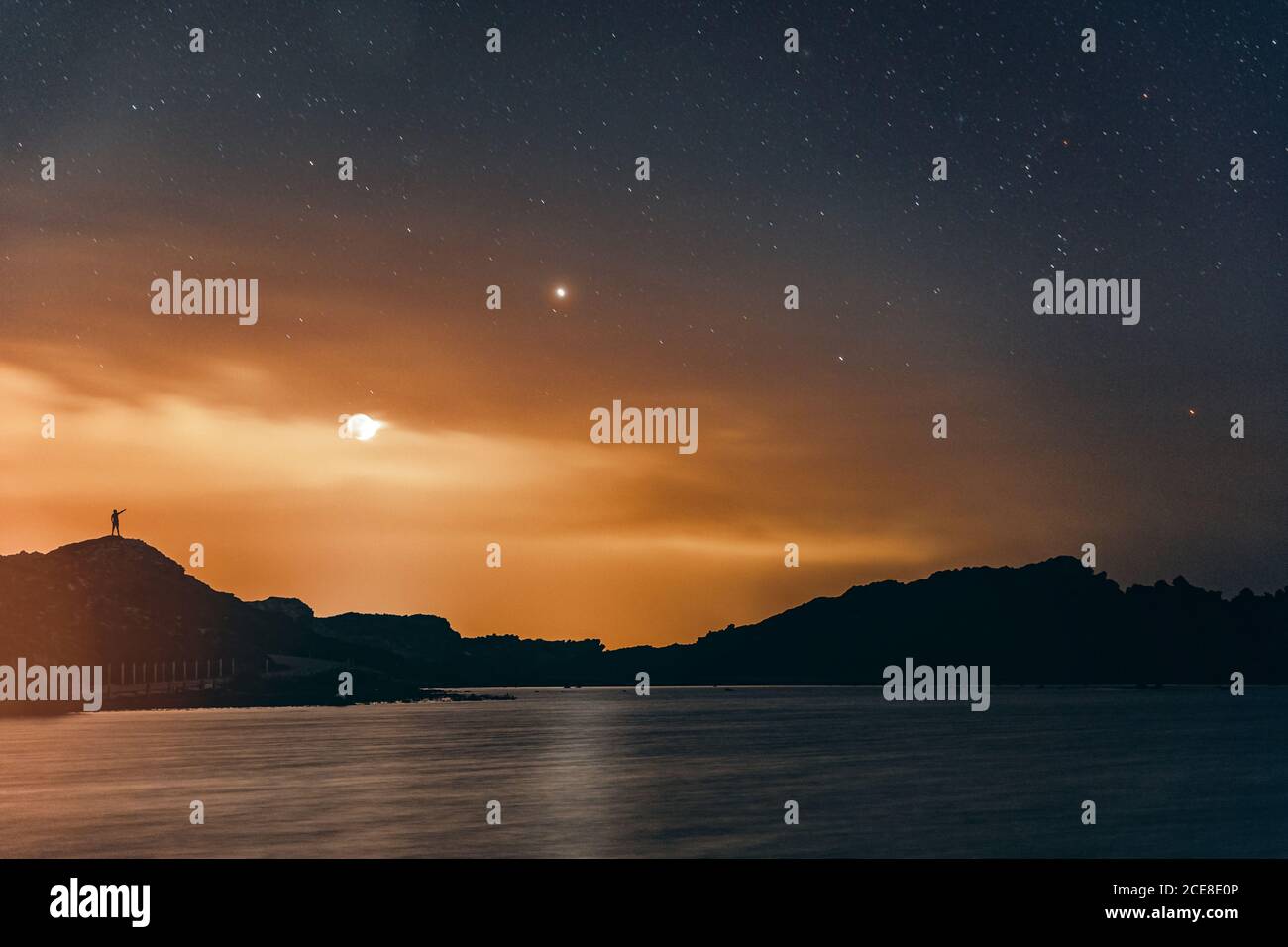 Silhouette di uomo che punta le stelle mentre osservano il Cielo notturno con la Luna e le stelle nel sfondo vicino al lago Foto Stock