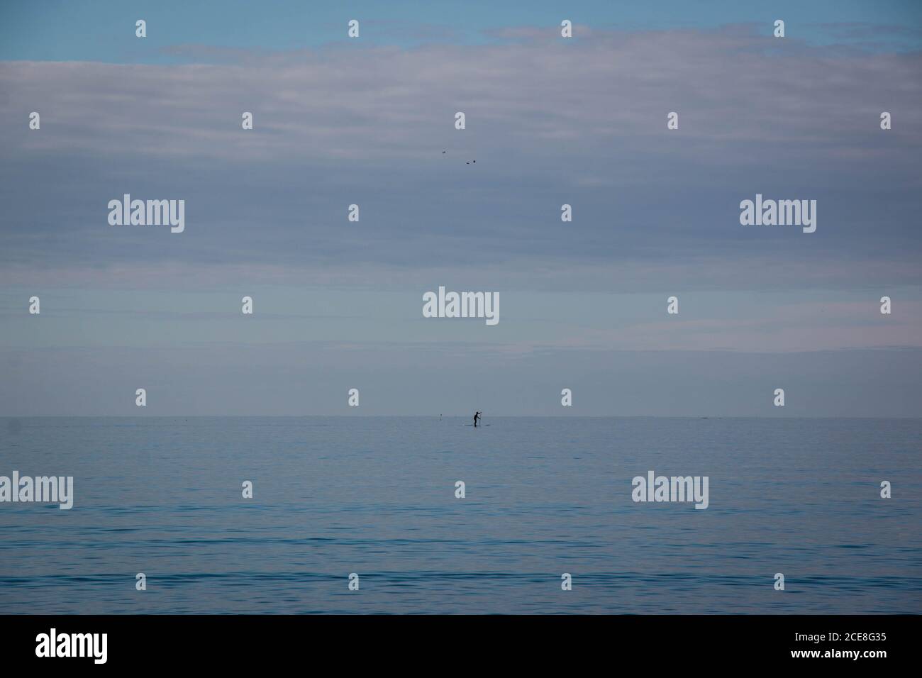 Indistinto paddleboarder all'orizzonte lontano con cielo blu nuvoloso Foto Stock