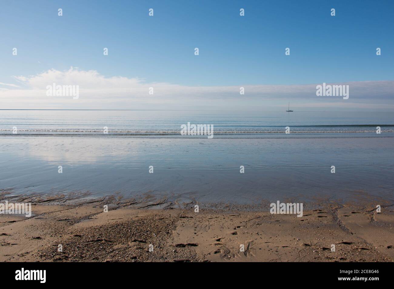 Nuvole nel cielo blu riflesse sulla spiaggia di sabbia in basso marea Foto Stock