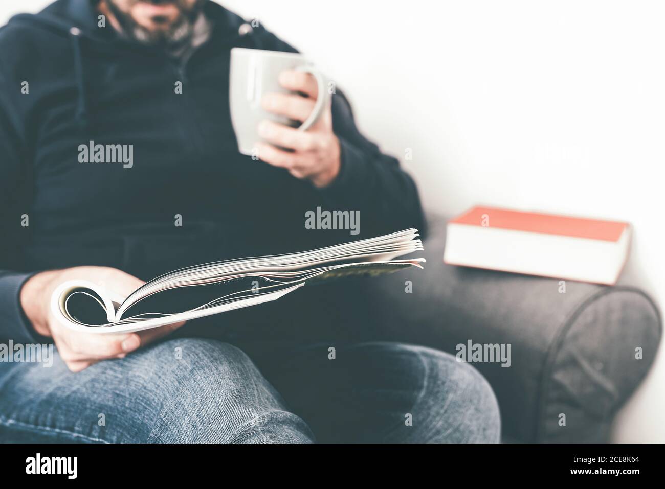 primo piano di uomo caucasico che legge rivista o giornale sul divano tenendo una tazza di caffè Foto Stock
