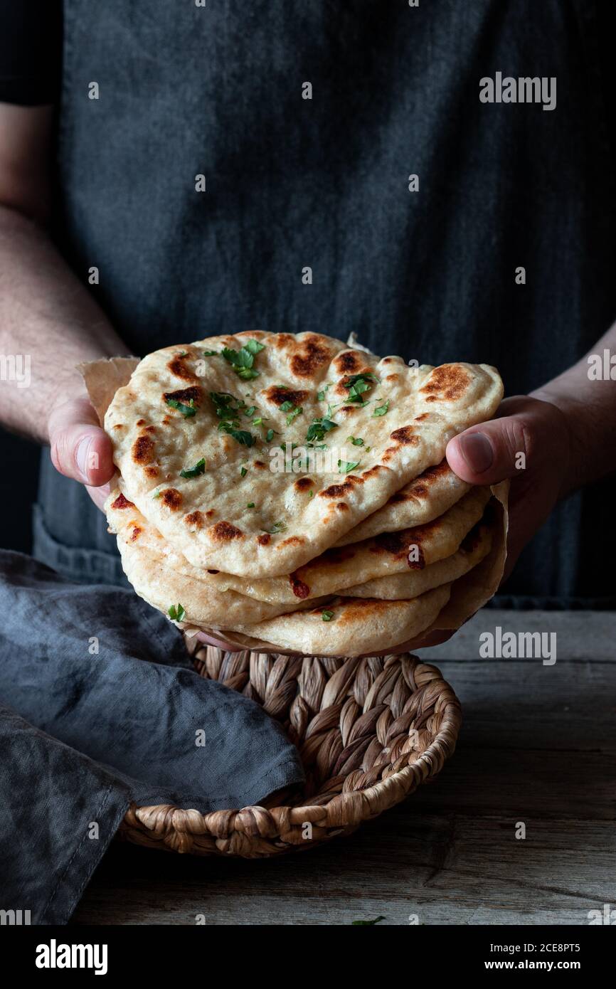Inriconoscibile panettiere maschile in grembiule con tradizionale pane di Naan guarnito con erbe Foto Stock