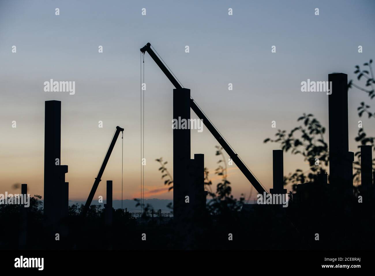 silhouette di cantiere con gru e colonne al tramonto Foto Stock