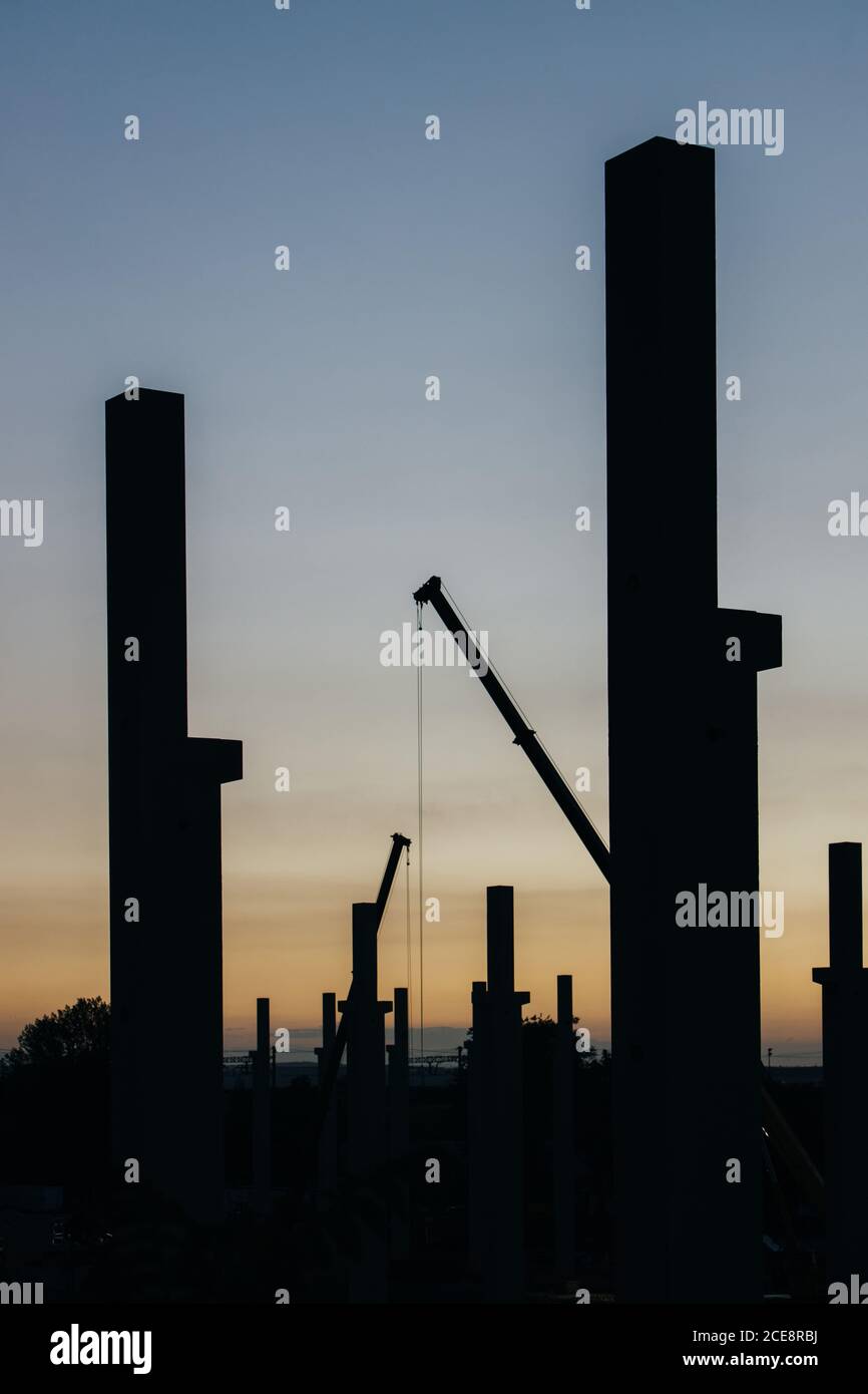 silhouette di cantiere con gru e colonne al tramonto Foto Stock