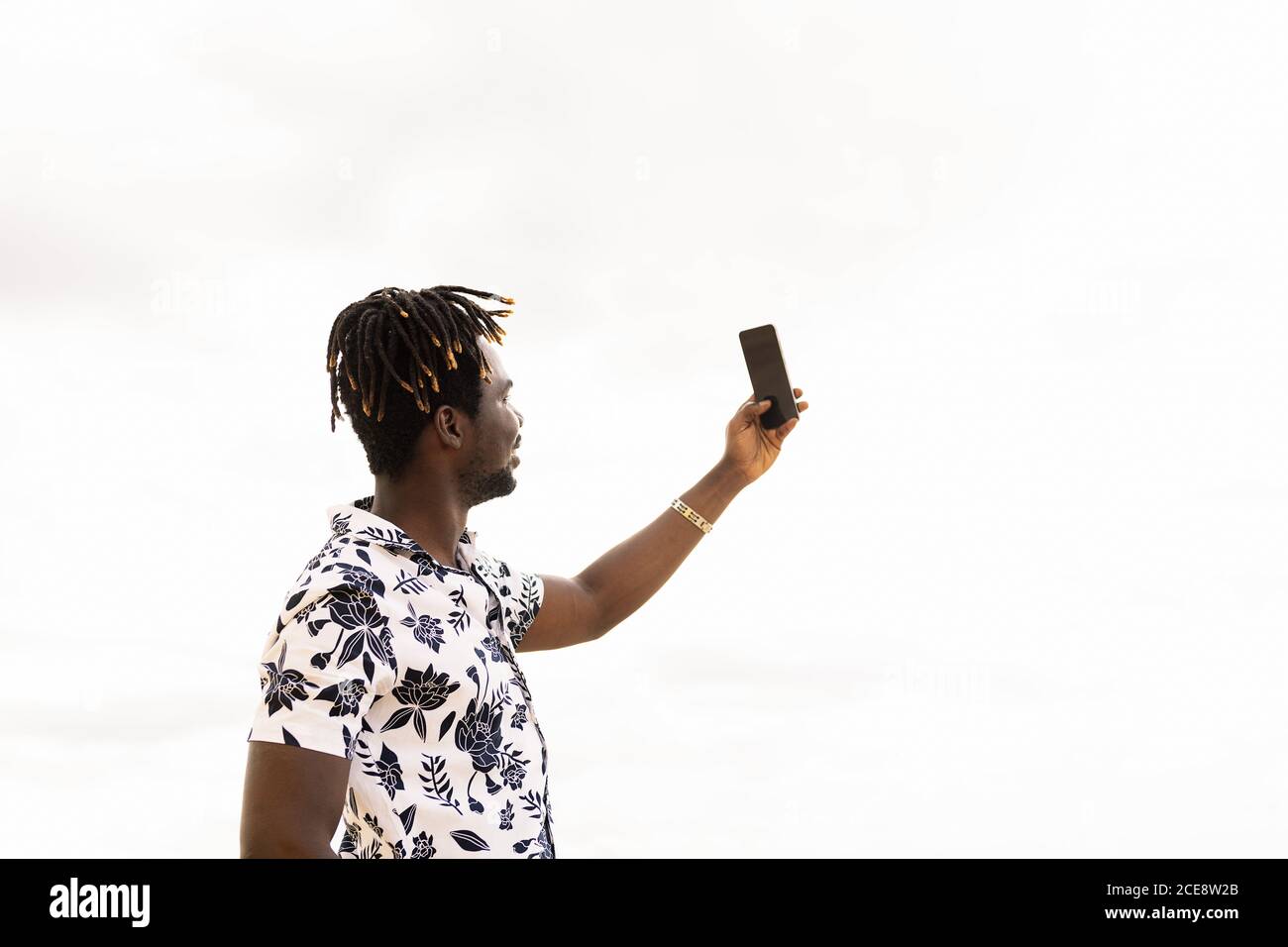 elegante giovane uomo nero scattare una foto selfie con il suo telefono cellulare con il cielo in background, tecnologia e stile di vita concetto, copia spazio per tex Foto Stock
