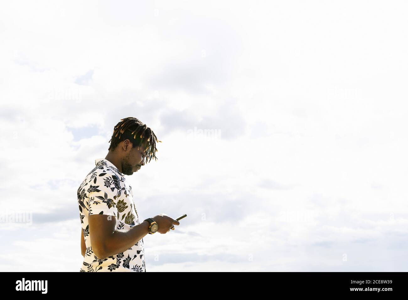 elegante giovane uomo nero che guarda il suo cellulare con il cielo in background, tecnologia e stile di vita concetto, copia spazio per tex Foto Stock