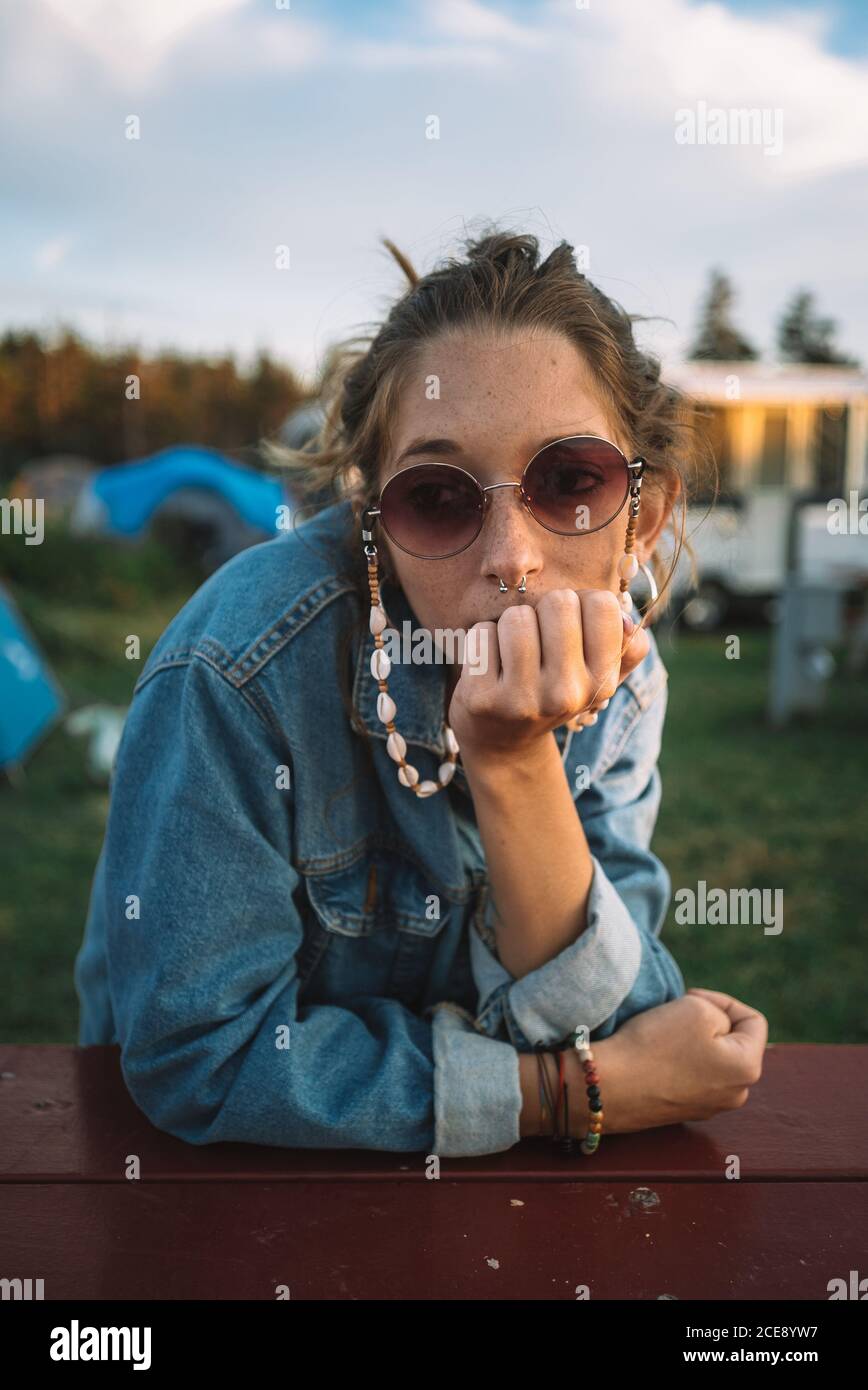 Hippie femminile tranquilla seduta a tavola di legno al campeggio e. vista tranquilla durante le vacanze estive Foto Stock