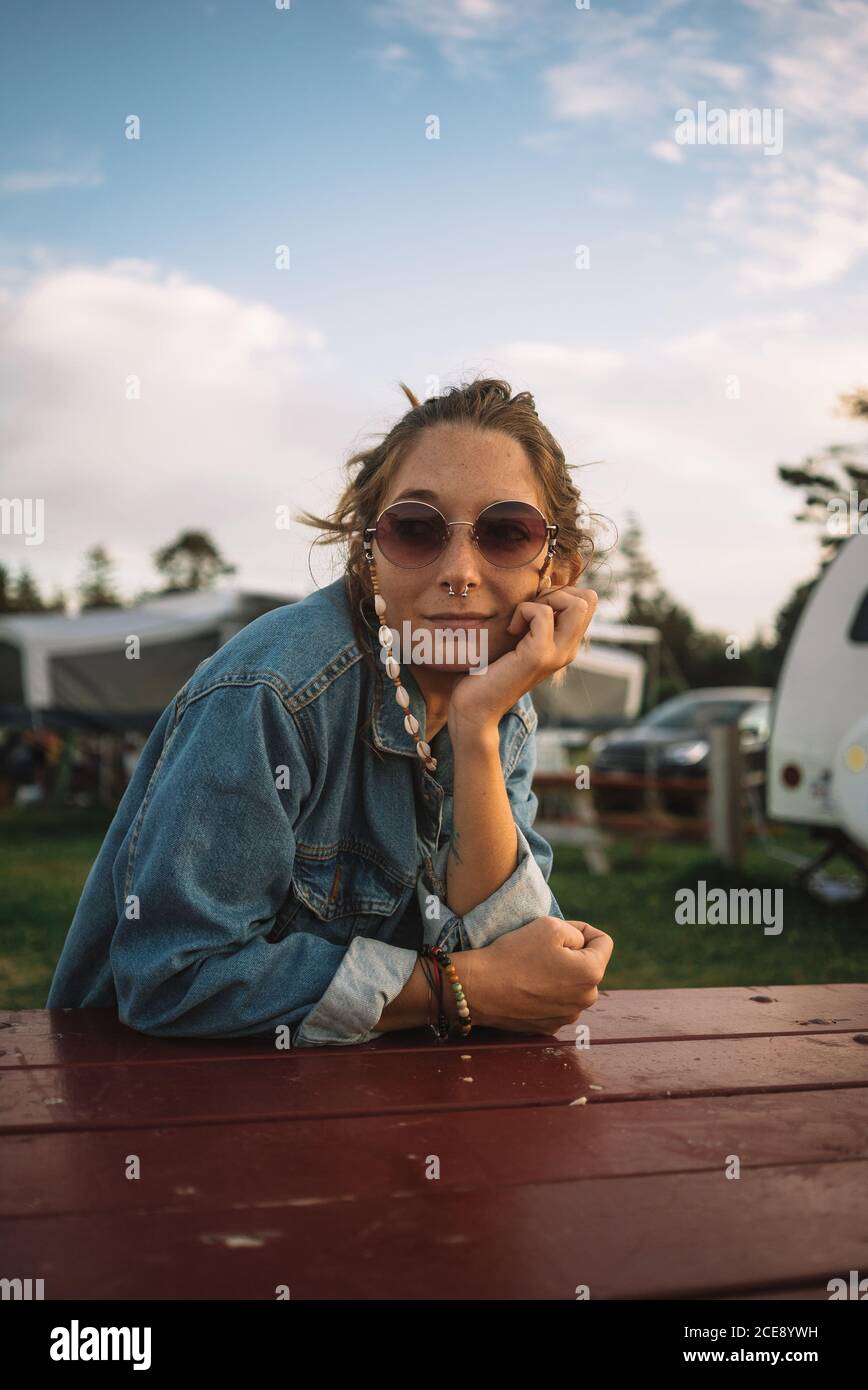 Hippie femminile tranquilla seduta a tavola di legno al campeggio e. vista tranquilla durante le vacanze estive Foto Stock