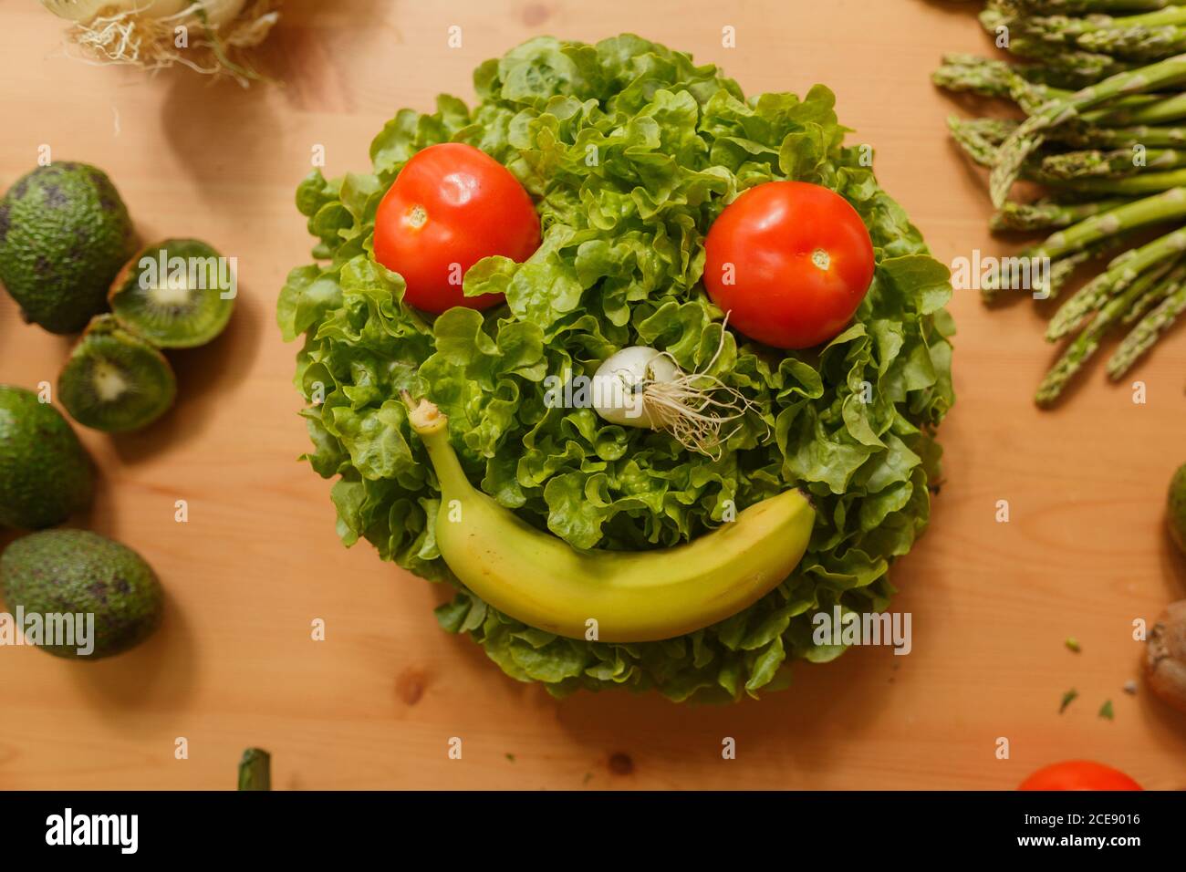 Da sopra composizione di frutta e verdura in forma di faccia sorridente sul tavolo in cucina Foto Stock