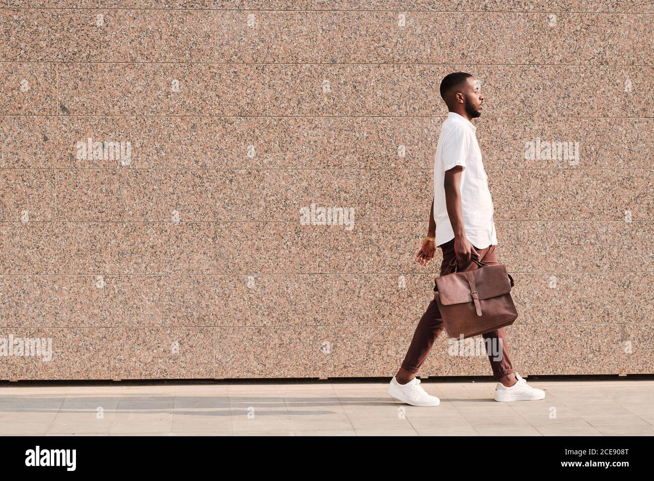 Vista laterale di un moderno uomo d'affari afro-americano con portafoglio a piedi sulla strada Foto Stock