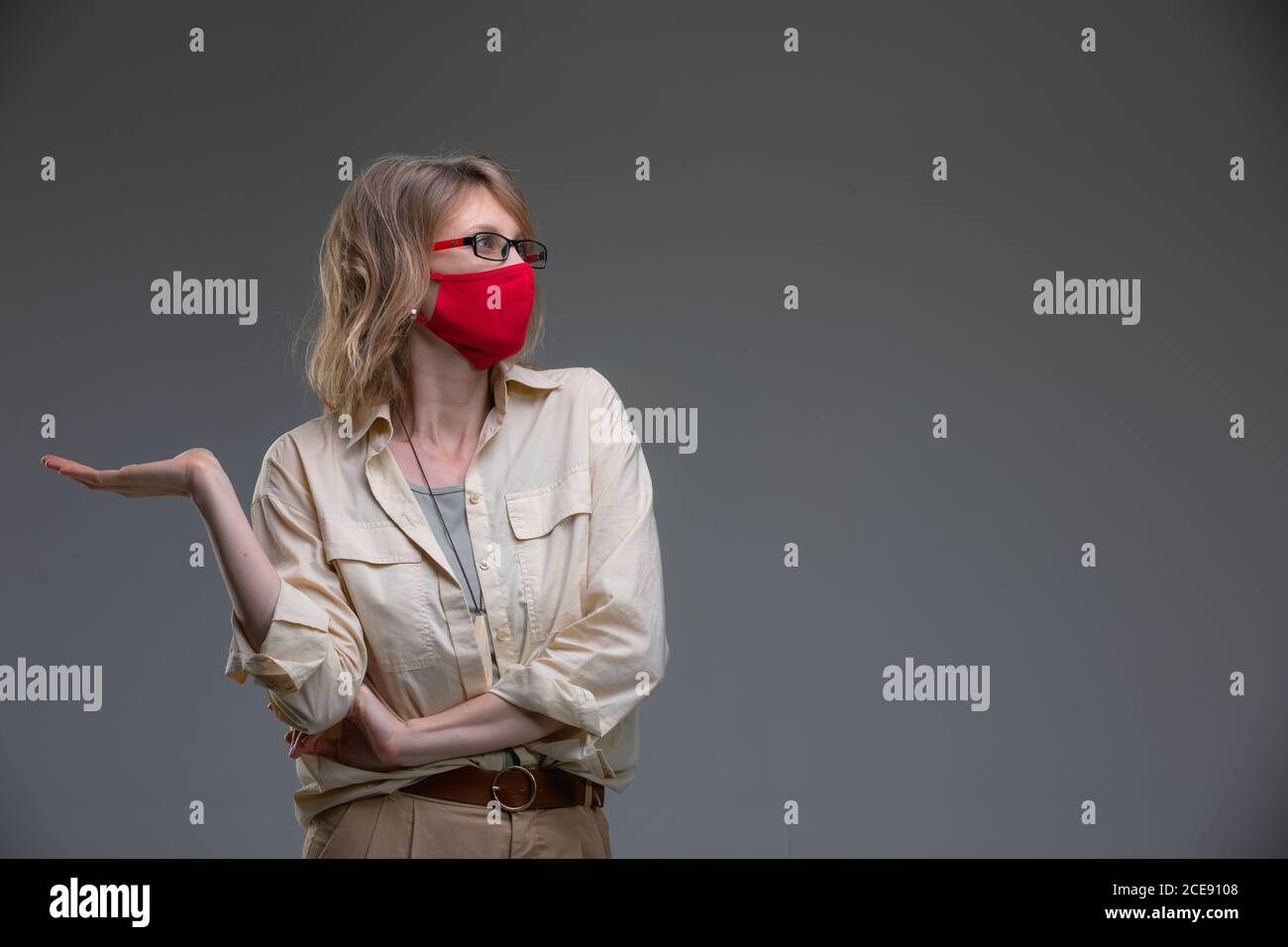 Bionda giovane femmina in rosso maschera protettiva contro i virus, tiene la testa. Foto Stock