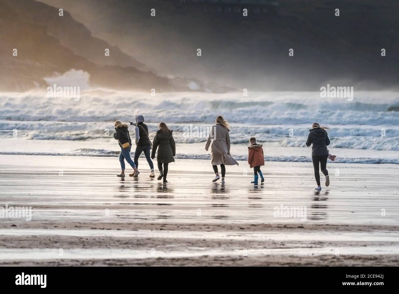Un gruppo di giovani vacanzieri che camminano in condizioni climatiche fredde e ventose attraverso Fistral Beach a Newquay in Cornovaglia. Foto Stock