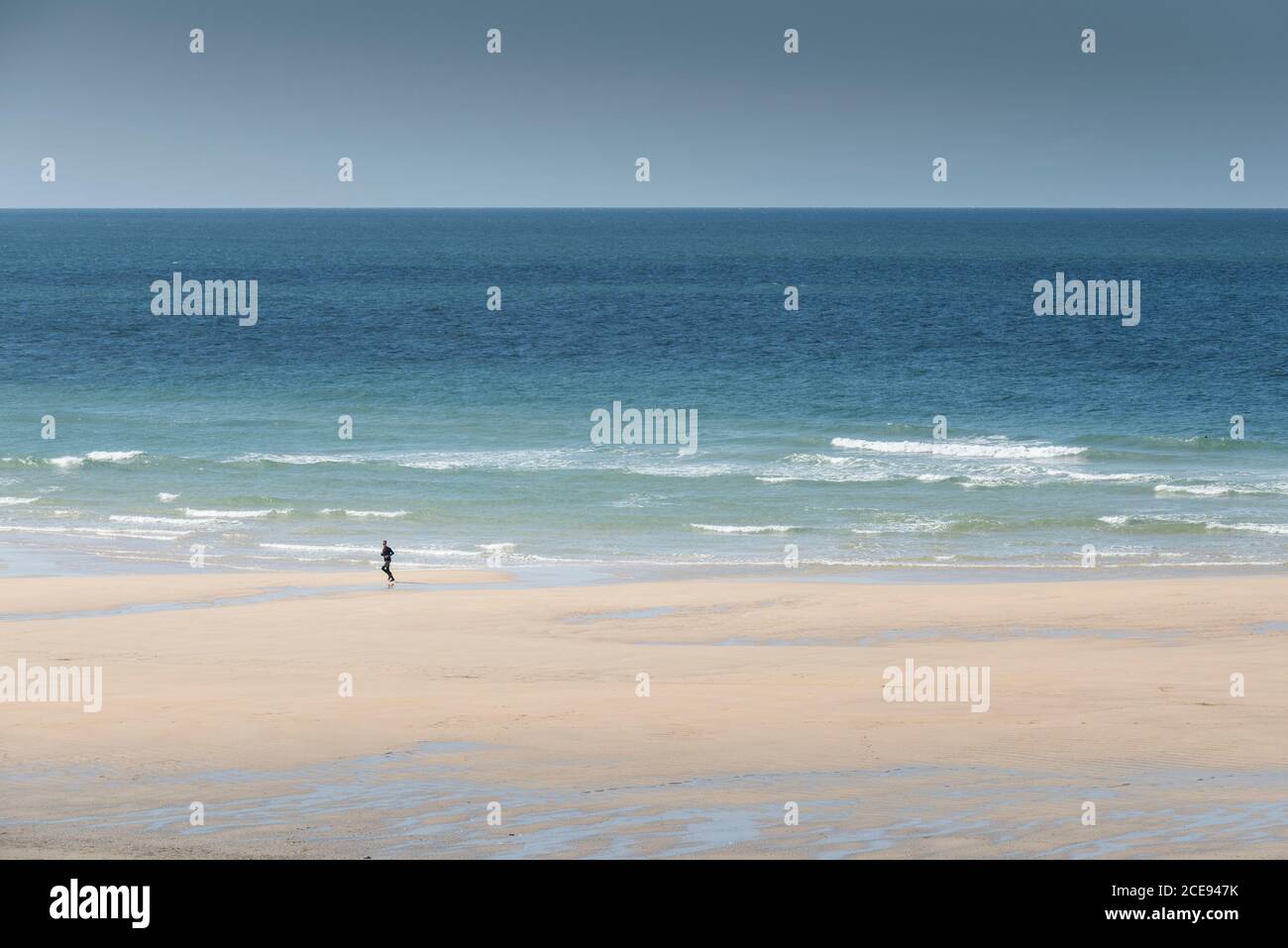 Una persona sola che corre lungo la riva di Fistral Beach a Newquay in Cornovaglia. Foto Stock