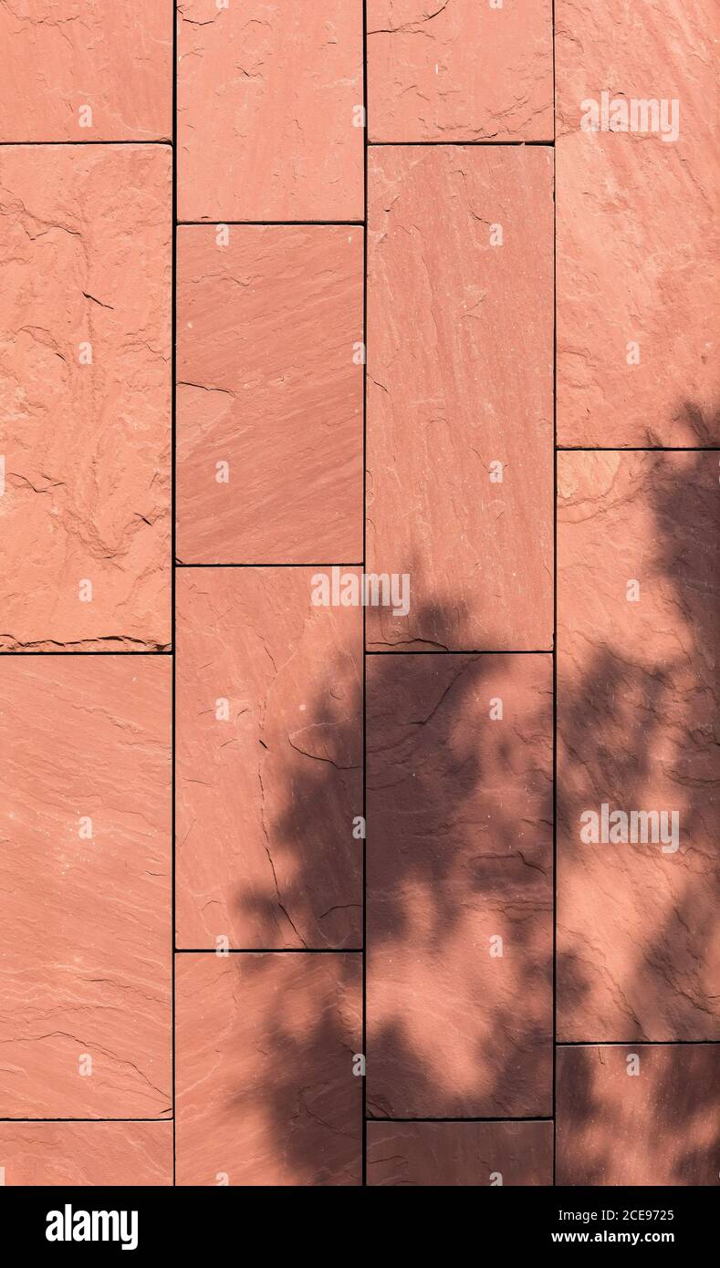 Una facciata di casa di lastre quadrate rosse in pietra naturale al sole con l'ombra di un albero. Foto Stock