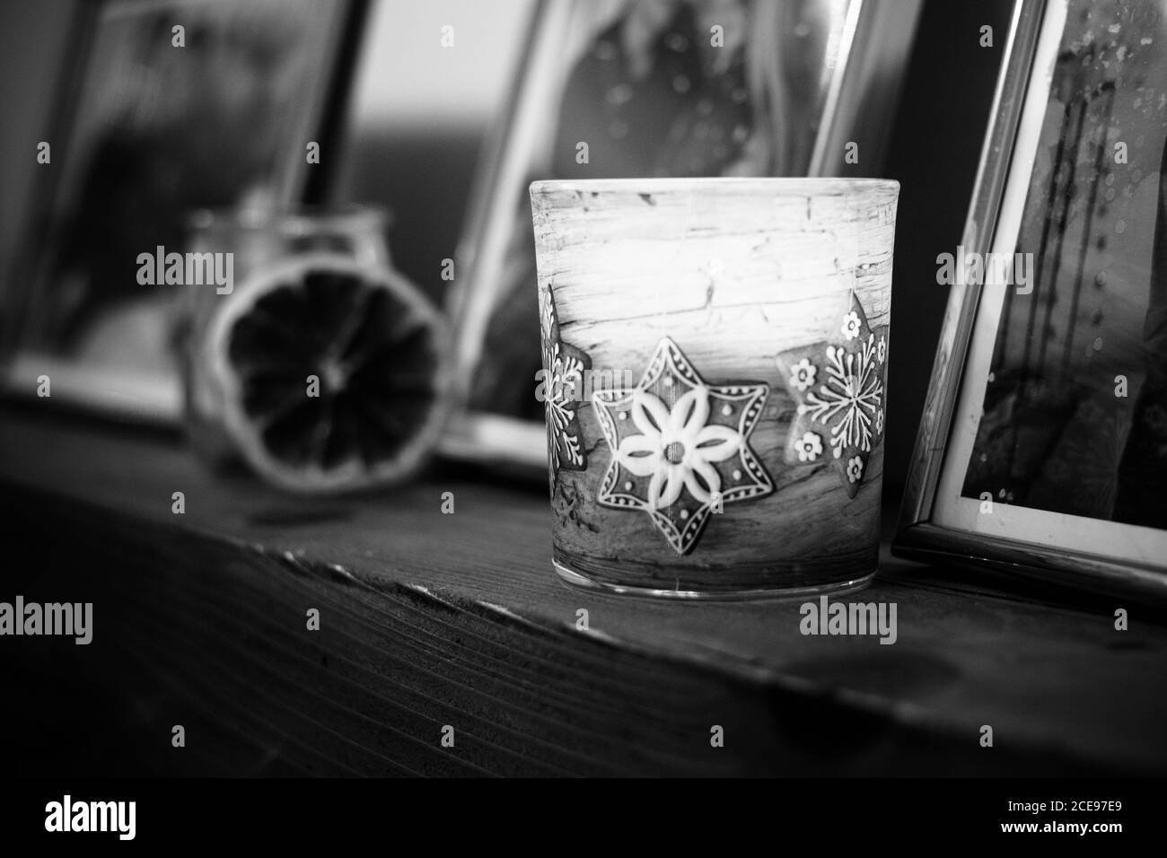 Scala di grigi ripresa di una candela a tema natalizio su vetro con sfondo sfocato Foto Stock