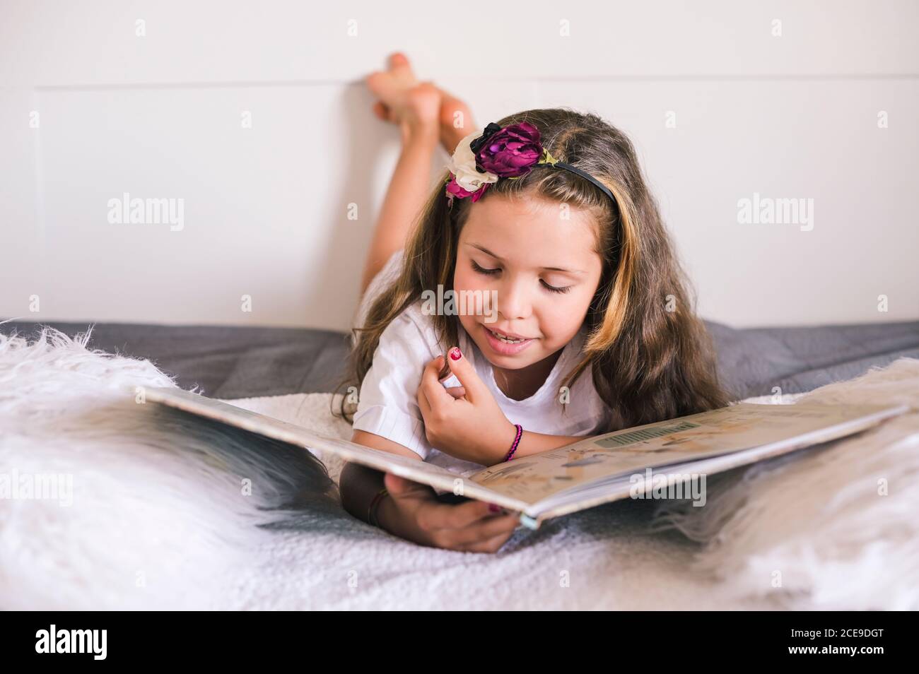 La studentessa sta leggendo. Bambina che legge un libro nella camera da letto sul letto. Educazione e hobby dei bambini. Colori diurni e luminosi. Spazio di copia. Alta qualità . Messa a fuoco morbida Foto Stock