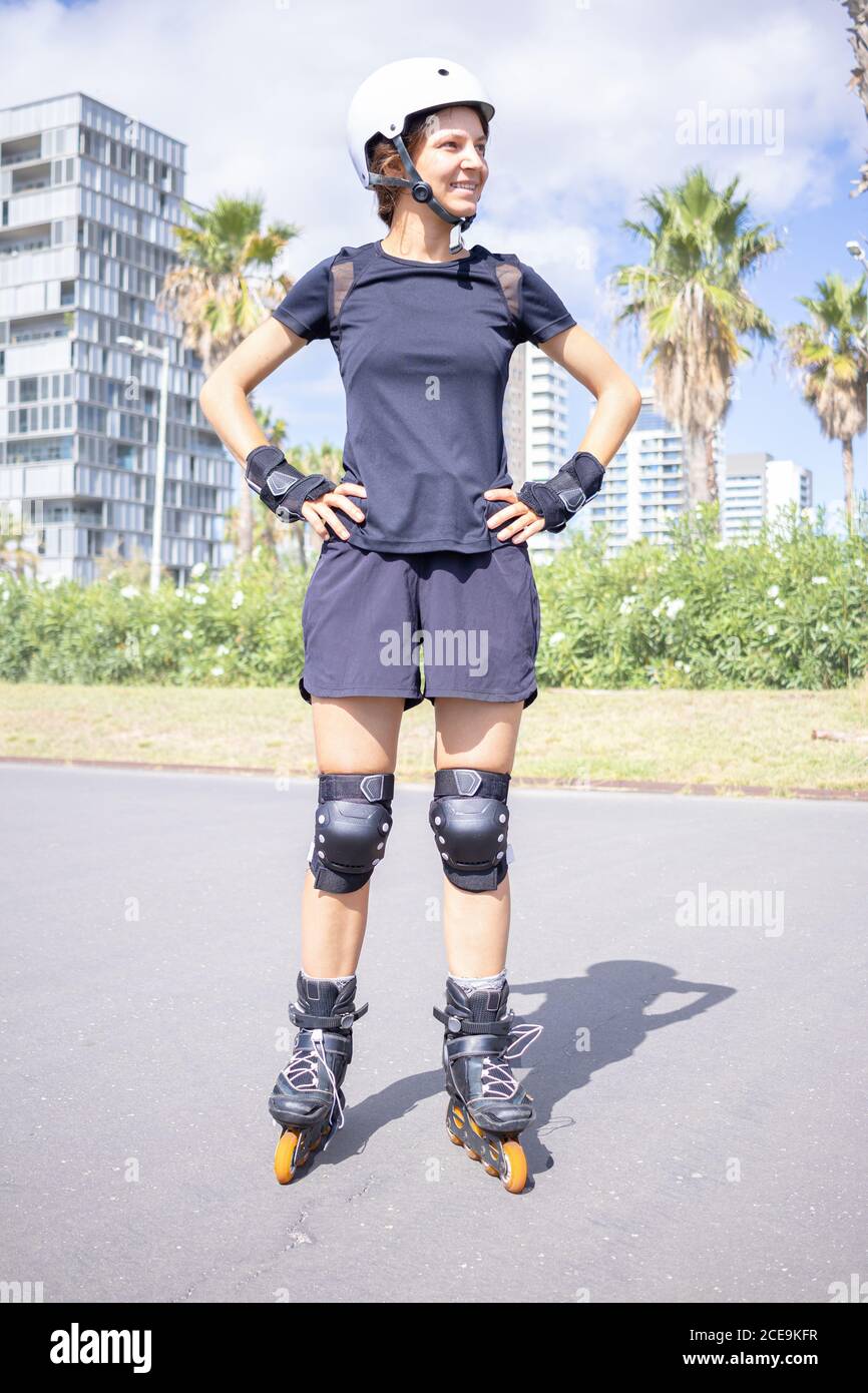 Giovane Felice pattinatore caucasico donna nel casco bianco e nero abiti sportivi, giornata di sole, skatepark, ambiente urbano. Foto Stock