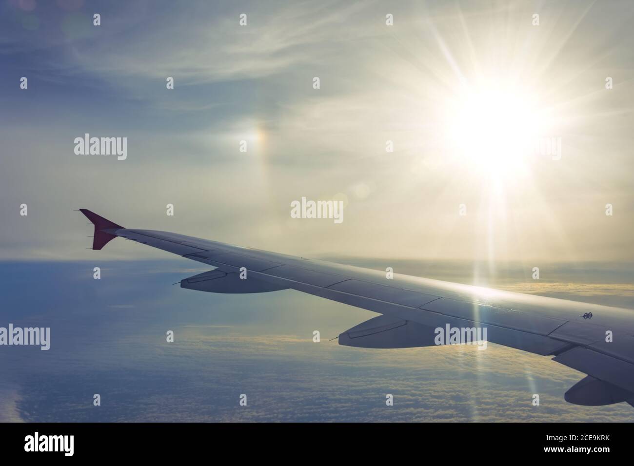 Vista dell'ala dell'aeroplano su un'altalena, nuvole soffici sullo skyline raggi di sole alone Foto Stock