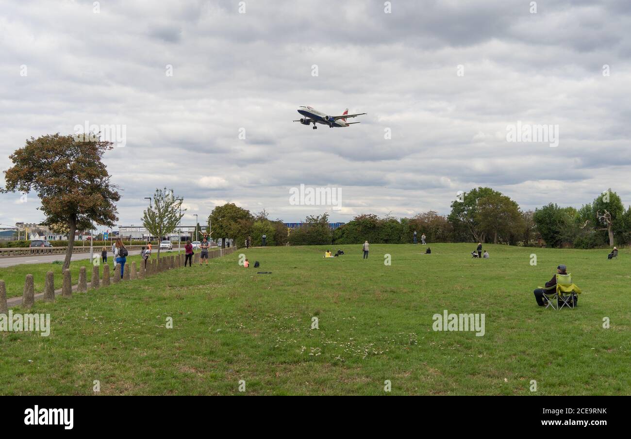 Gli appassionati di volo si siedono sull'erba guardando un aereo atterra dall'aeroporto di Heathrow. Foto Stock