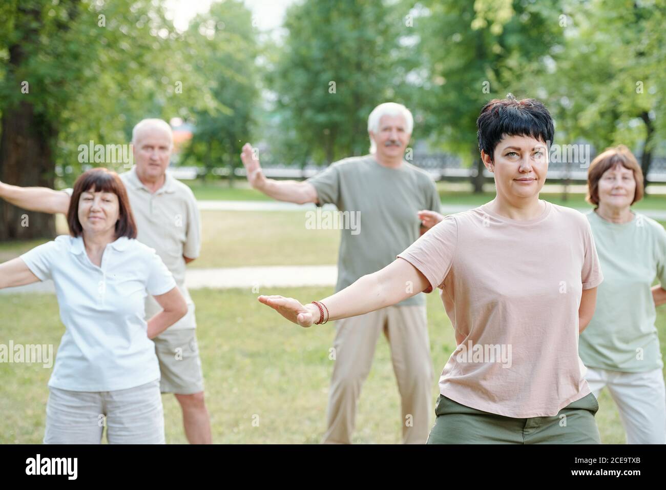 Persone attive mature in piedi in parco e spostare le braccia a. qigong pratica Foto Stock