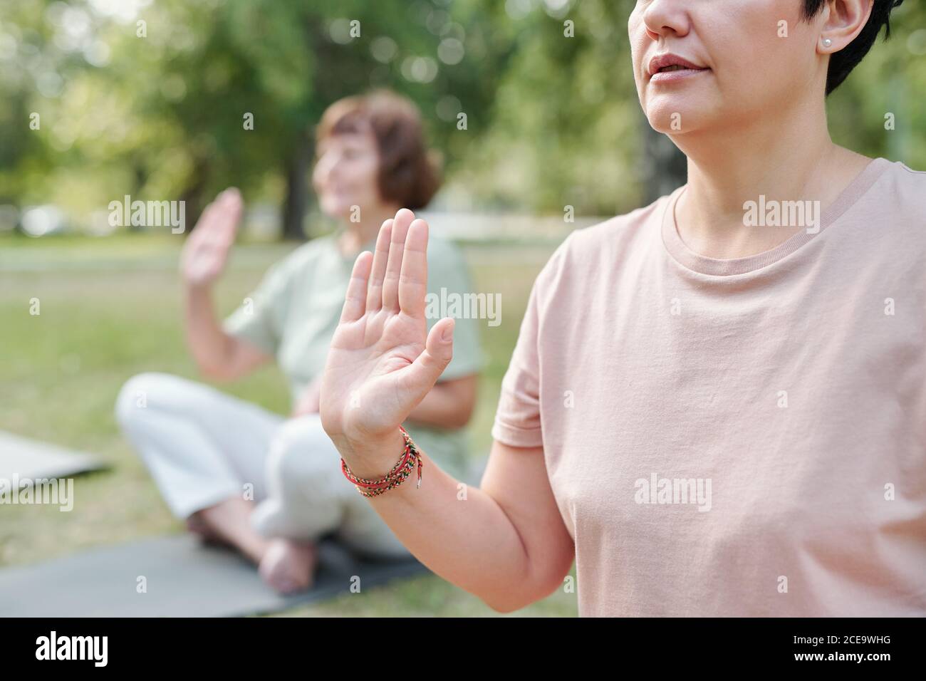 Primo piano di donne che si siedono in asana all'aperto e che eseguono esercizi di yoga, che tengono le mani come voti Foto Stock
