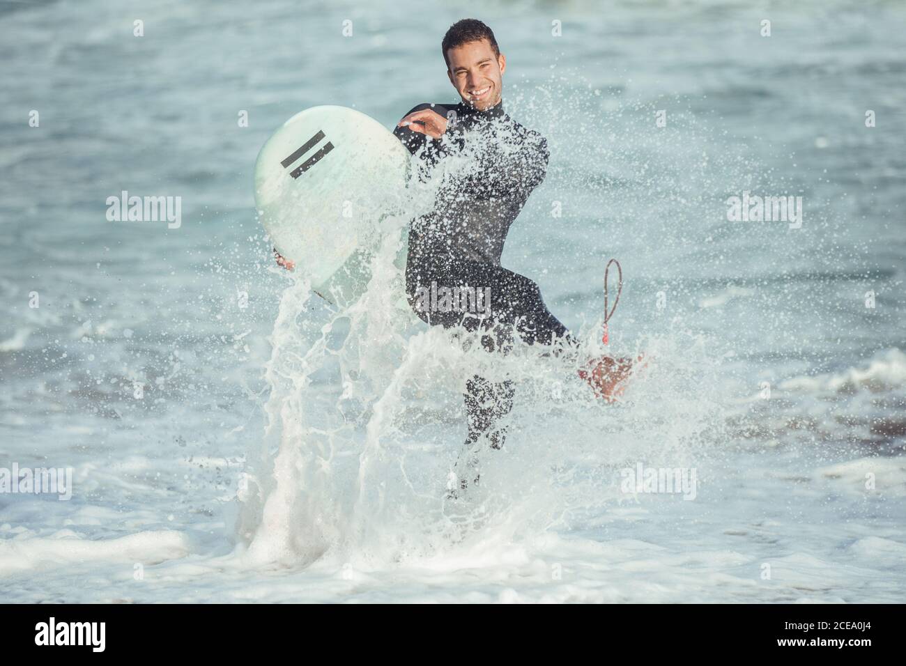 Elettrizzato uomo sportivo con tavola da surf che spruzzi d'acqua e ridendo alla macchina fotografica alla luce del sole, Barcellona Foto Stock