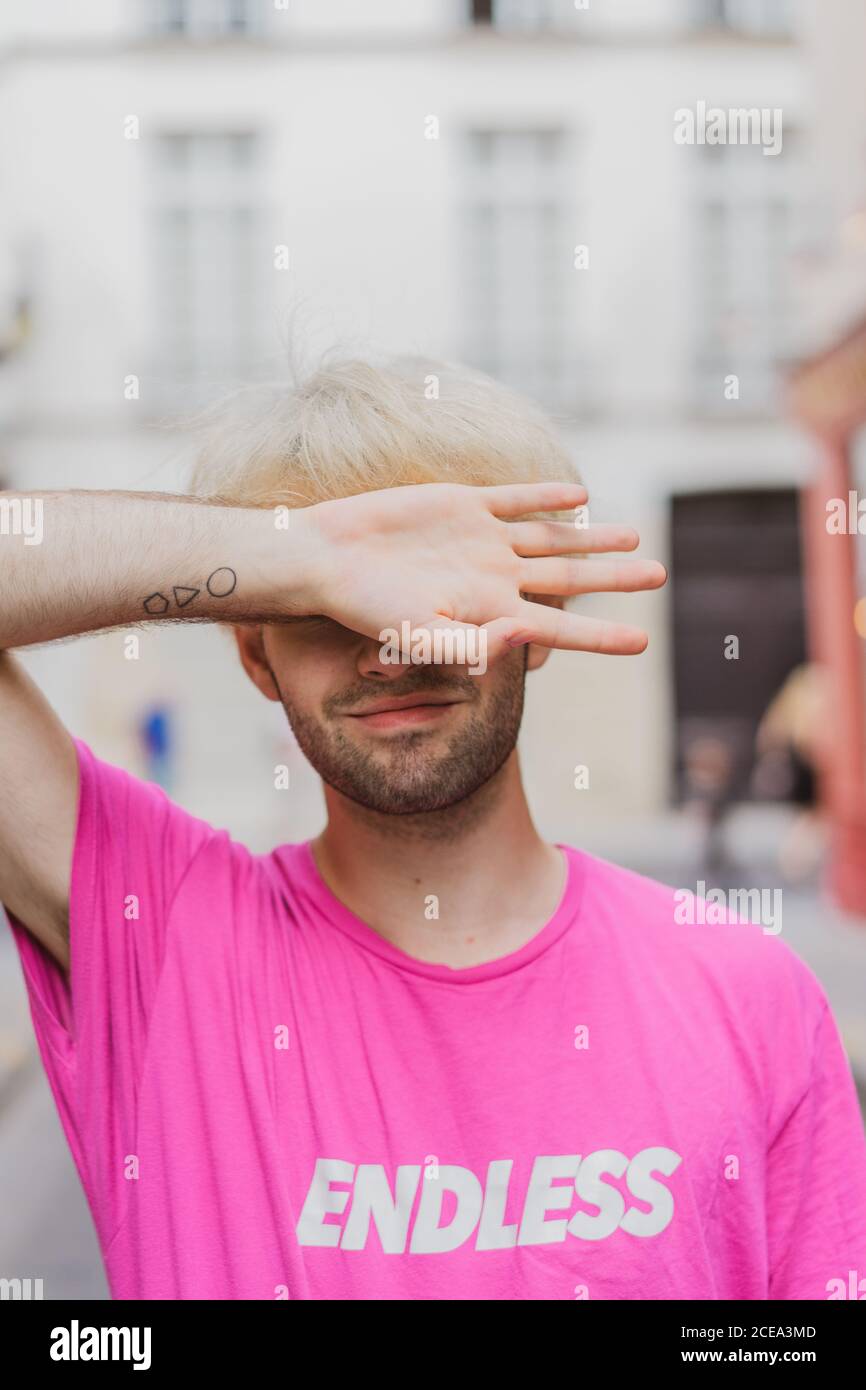 Uomo trendy con bearded con pettinetta di moda che indossa t-shirt rosa strada su sfondo sfocato Foto Stock