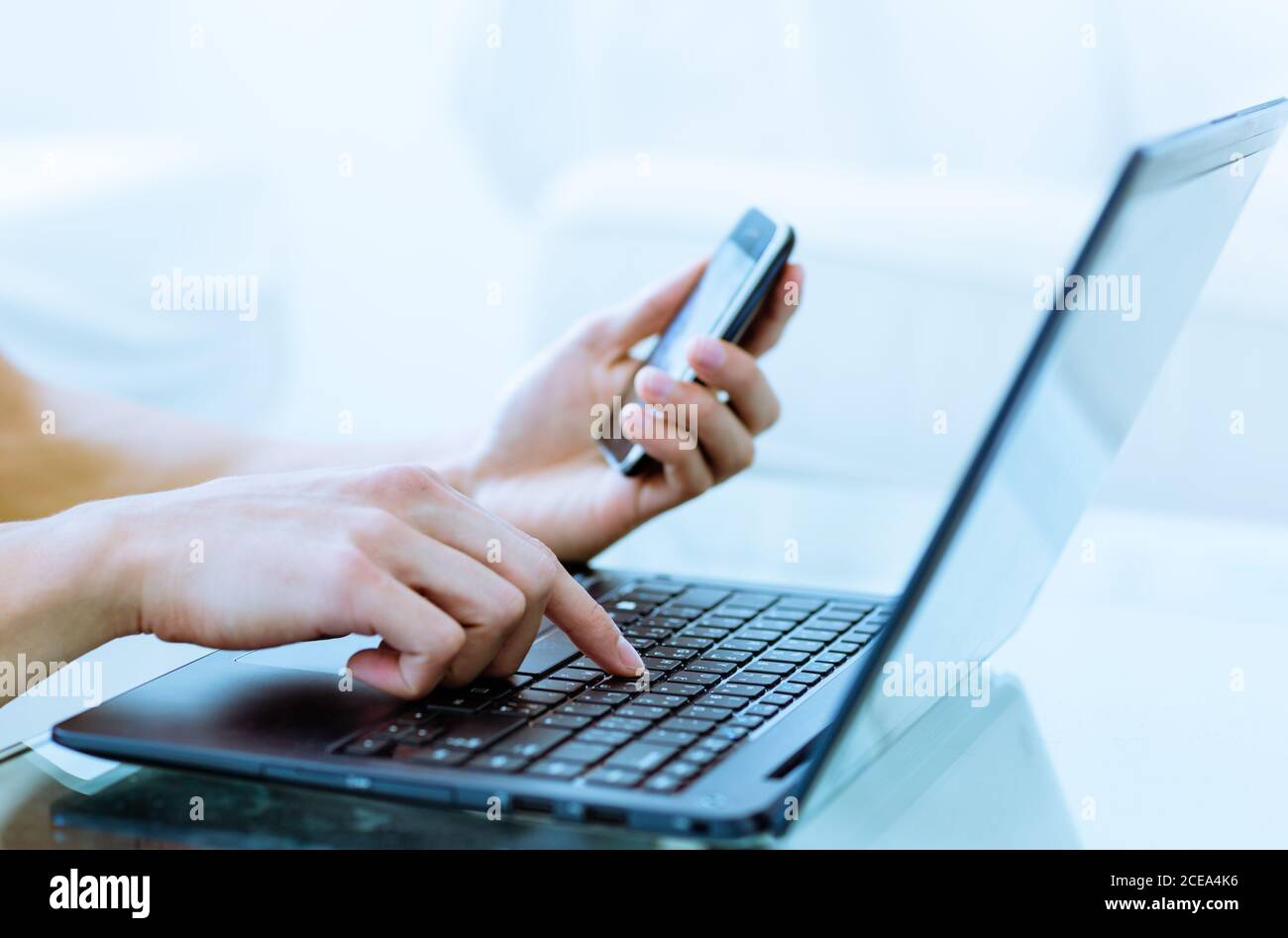 Primo piano della digitazione delle mani su un computer portatile online mentre si tiene un telefono cellulare a casa. Foto Stock