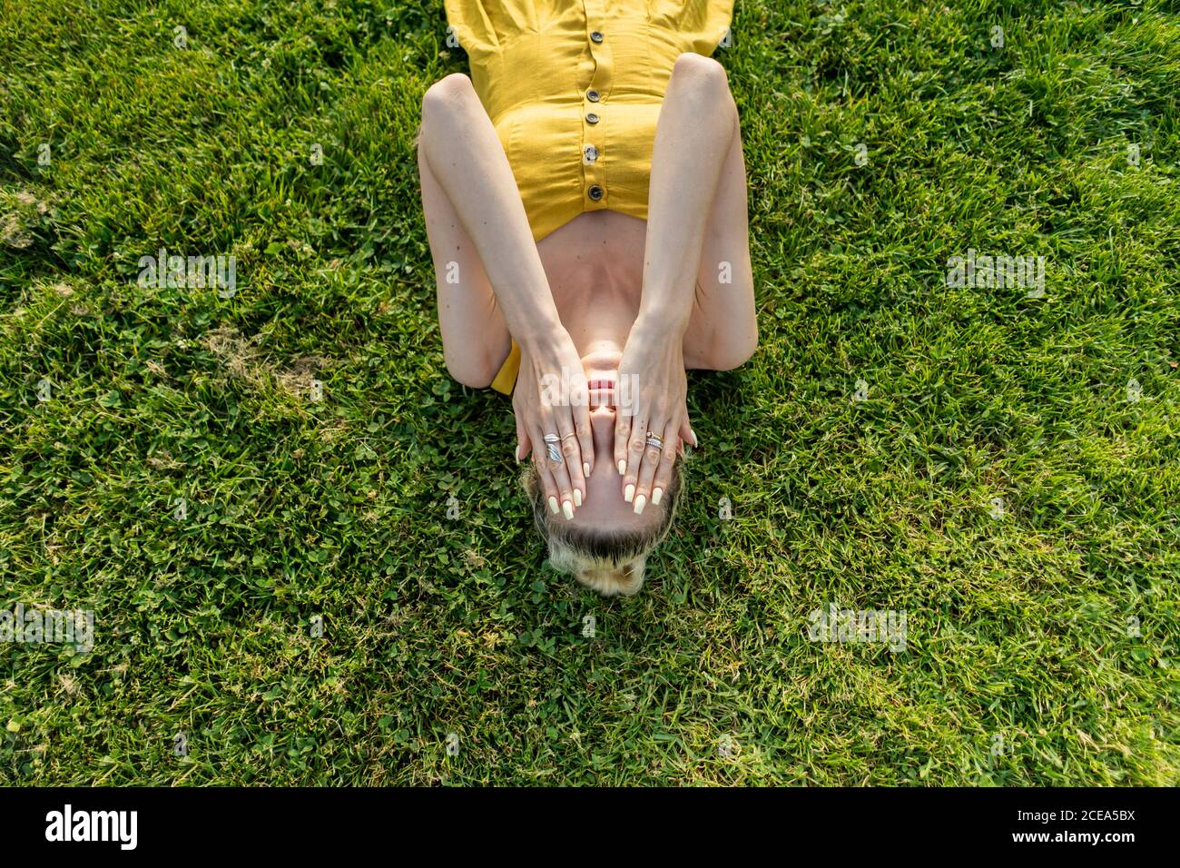 Donna sdraiata sull'erba con le mani sul viso Foto Stock