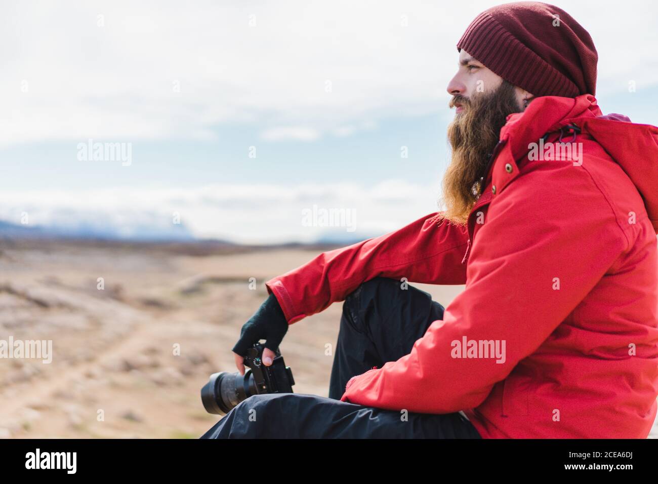 Vista laterale del maschio bearded in abiti caldi seduti sopra Spettacolare sfondo di aridi paesaggi islandesi in Namaskardh Foto Stock