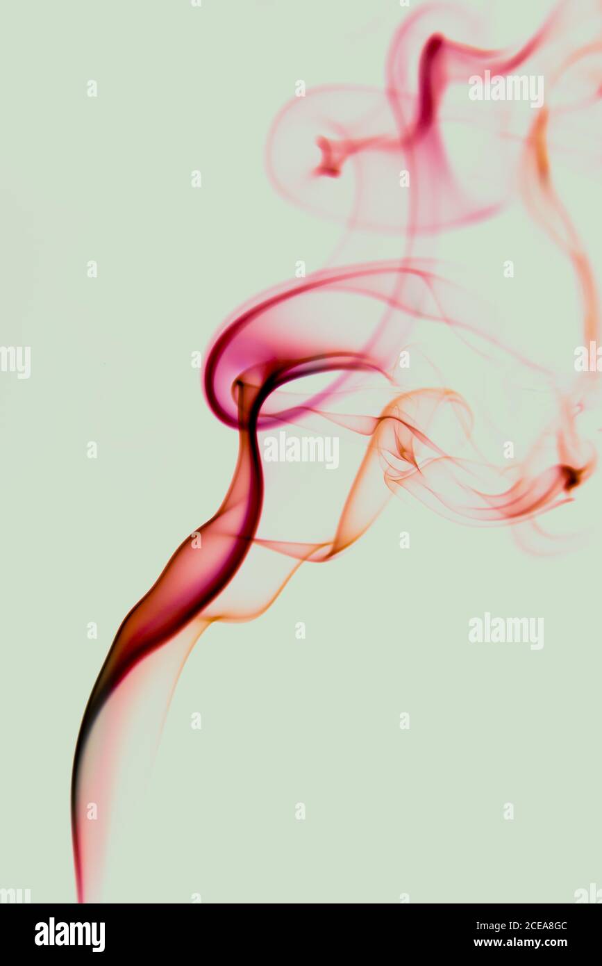 Riccioli di sottile rosso vorticoso di fumo su sfondo verde chiaro Foto Stock