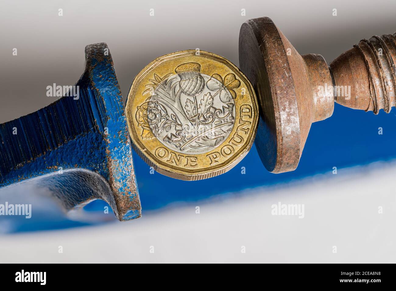 Concetto per lo stress finanziario o la recessione con il Regno Unito una libbra moneta di sterling che è schiacciata tra le mascelle di un grande vizio. Immagine macro dettagliata della morsa Foto Stock